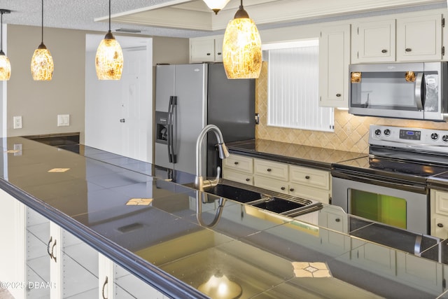 kitchen featuring appliances with stainless steel finishes, white cabinetry, a sink, and decorative light fixtures