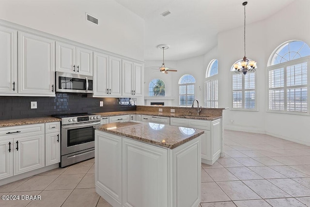 kitchen with appliances with stainless steel finishes, ceiling fan with notable chandelier, light tile patterned floors, pendant lighting, and a center island