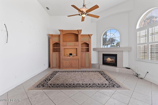 living room featuring a towering ceiling, ceiling fan, a fireplace, and light tile patterned floors