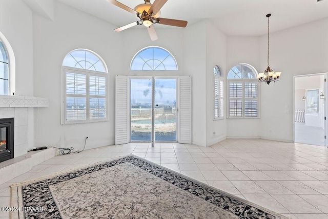 tiled living room featuring a towering ceiling, ceiling fan with notable chandelier, and a tiled fireplace