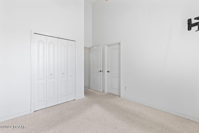 unfurnished bedroom with light colored carpet, a towering ceiling, and a closet