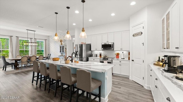 kitchen featuring a kitchen island with sink, light stone countertops, stainless steel appliances, and a breakfast bar