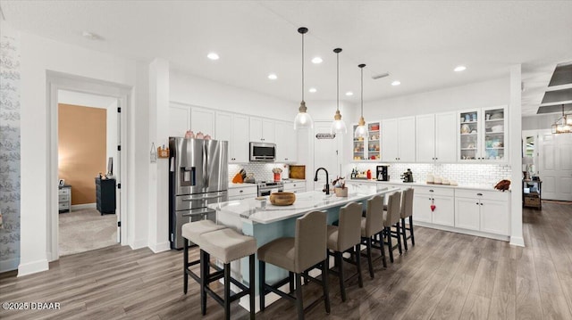 kitchen featuring appliances with stainless steel finishes, hanging light fixtures, a center island with sink, and white cabinets