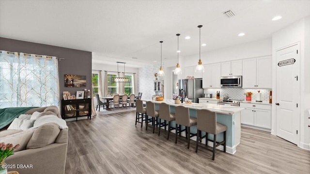 kitchen with a breakfast bar, white cabinetry, hanging light fixtures, a center island with sink, and appliances with stainless steel finishes