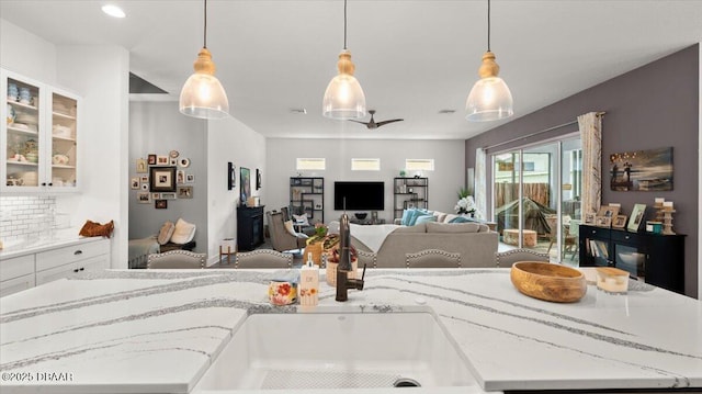 kitchen with tasteful backsplash, light stone countertops, a kitchen island with sink, and decorative light fixtures