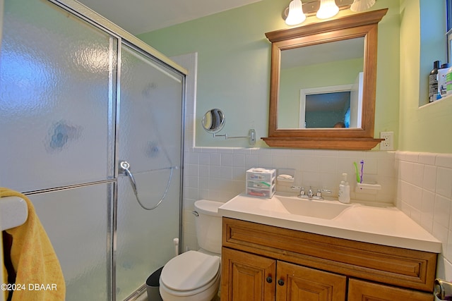 bathroom featuring a stall shower, wainscoting, toilet, vanity, and tile walls