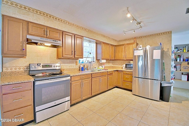 kitchen featuring light tile patterned floors, brown cabinetry, appliances with stainless steel finishes, under cabinet range hood, and a sink