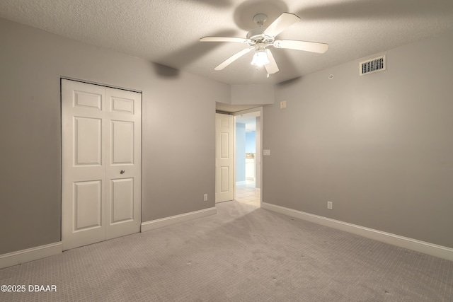 unfurnished bedroom featuring a closet, light carpet, a textured ceiling, baseboards, and visible vents