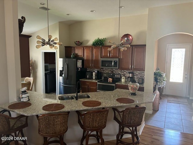 kitchen featuring sink, appliances with stainless steel finishes, light hardwood / wood-style flooring, lofted ceiling, and decorative backsplash