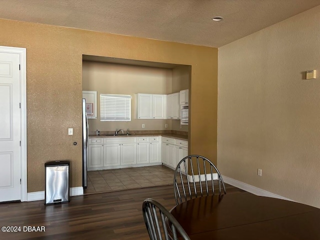 kitchen with dark wood-type flooring, a textured ceiling, sink, white cabinetry, and stainless steel fridge