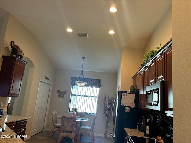 kitchen with stainless steel appliances, lofted ceiling, dark brown cabinetry, light stone countertops, and decorative light fixtures