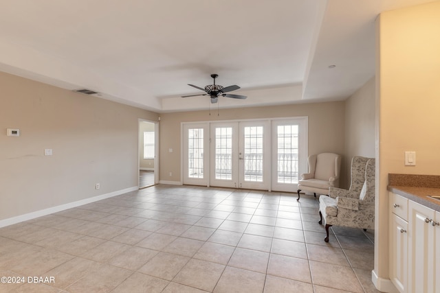 living area with ceiling fan, light tile patterned floors, and a tray ceiling