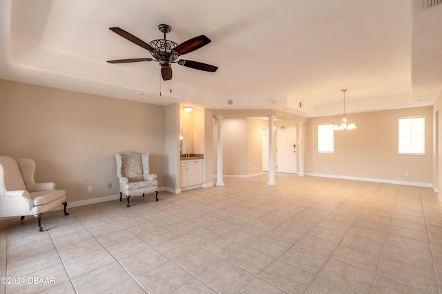 unfurnished room with a tray ceiling, sink, ornate columns, and ceiling fan with notable chandelier