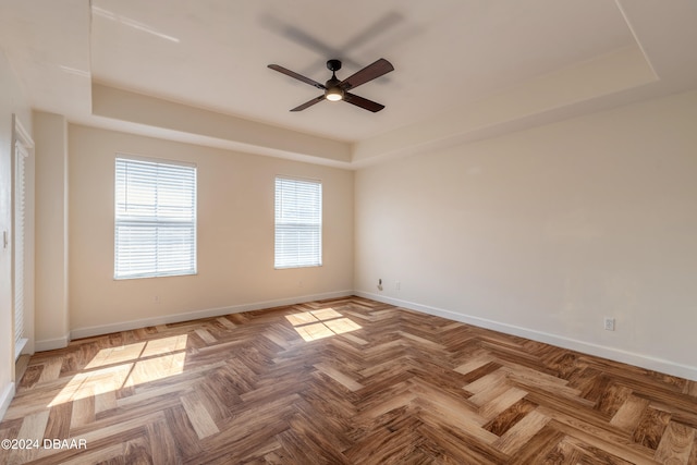 empty room with parquet flooring, ceiling fan, and a tray ceiling