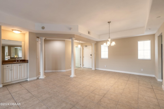 tiled spare room featuring ornate columns, a chandelier, a raised ceiling, and sink