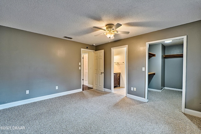 unfurnished bedroom featuring a walk in closet, visible vents, carpet flooring, ensuite bath, and baseboards