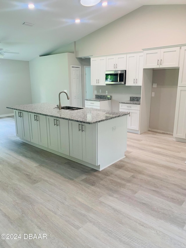 kitchen with a kitchen island with sink, white cabinetry, and lofted ceiling