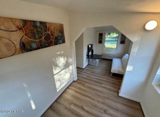 hallway featuring baseboards, vaulted ceiling, and wood finished floors