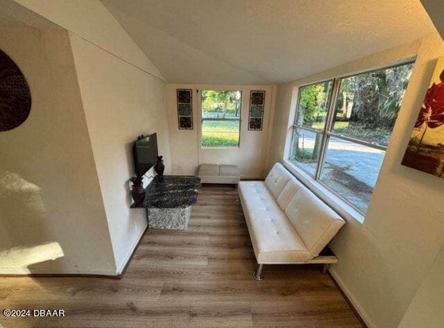 living area with vaulted ceiling, baseboards, and wood finished floors