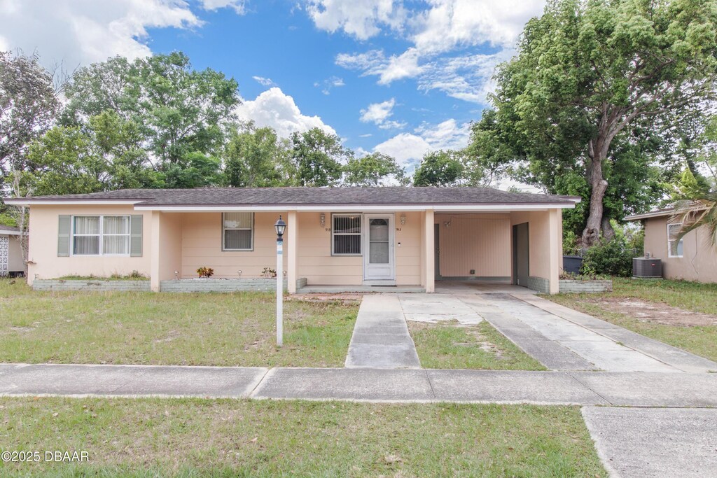ranch-style home featuring a front lawn, a carport, cooling unit, and driveway