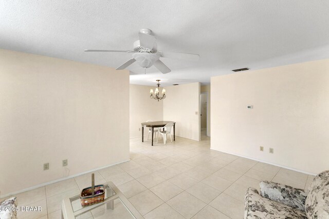 empty room with light tile patterned flooring, ceiling fan with notable chandelier, visible vents, and a textured ceiling