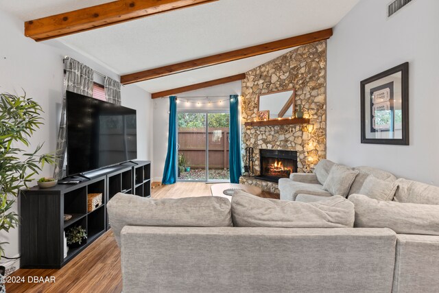 living room with light hardwood / wood-style floors, a stone fireplace, and vaulted ceiling with beams