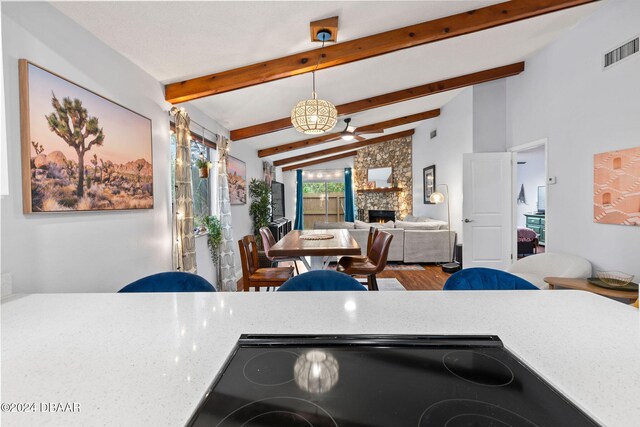 kitchen featuring ceiling fan, pendant lighting, a fireplace, black stove, and lofted ceiling with beams