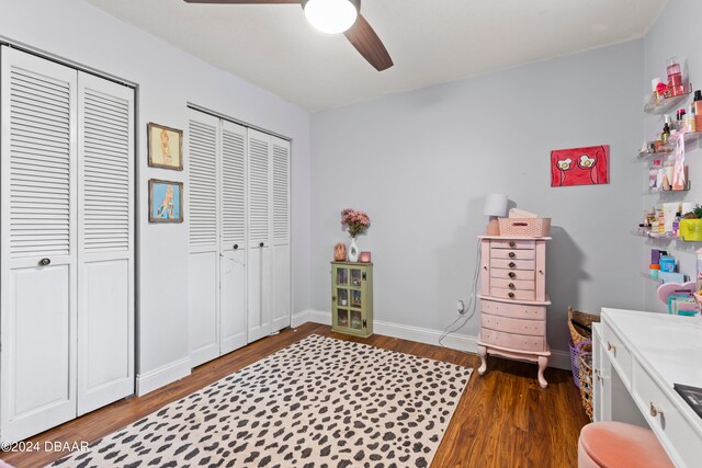 bedroom with dark hardwood / wood-style flooring, ceiling fan, and two closets