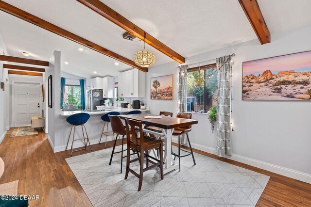 dining space with lofted ceiling with beams and light hardwood / wood-style floors