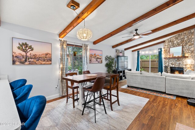 dining room featuring light wood-type flooring, ceiling fan, vaulted ceiling with beams, and a fireplace