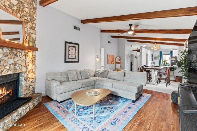 living room with dark wood-type flooring, lofted ceiling with beams, a stone fireplace, and ceiling fan