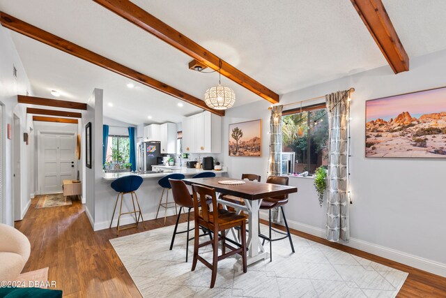 dining space with light hardwood / wood-style flooring and vaulted ceiling with beams