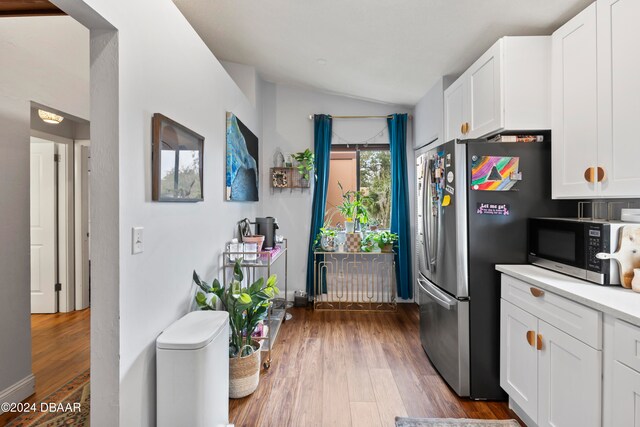 kitchen with white cabinets, hardwood / wood-style floors, vaulted ceiling, and stainless steel appliances