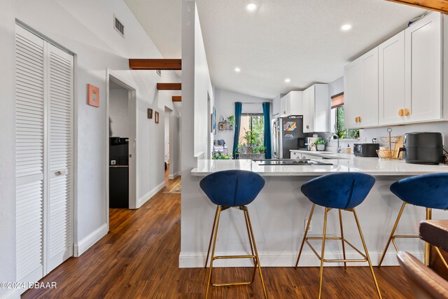 kitchen featuring lofted ceiling, dark wood-type flooring, a kitchen breakfast bar, white cabinetry, and appliances with stainless steel finishes