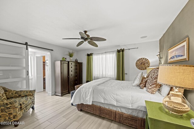 bedroom featuring light wood-type flooring, a barn door, and ceiling fan