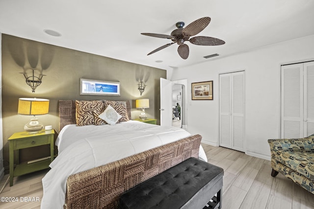 bedroom featuring light wood-type flooring, ceiling fan, and multiple closets