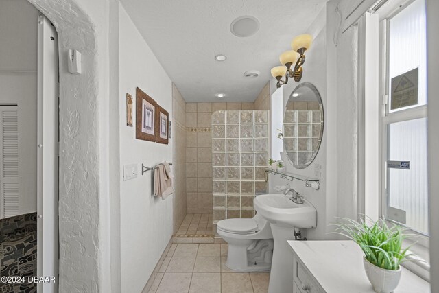 bathroom featuring tiled shower, toilet, tile patterned floors, tile walls, and sink