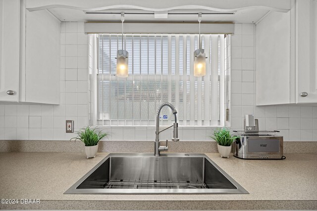 kitchen featuring decorative light fixtures, backsplash, sink, and white cabinets