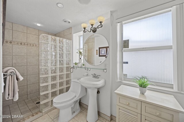 bathroom featuring tile patterned flooring, toilet, a textured ceiling, and tiled shower