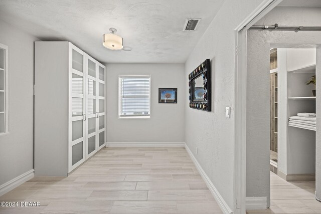 hall with light wood-type flooring and a textured ceiling