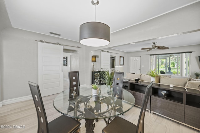 dining space with light hardwood / wood-style flooring, a barn door, and ceiling fan