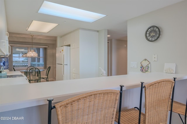 kitchen featuring white cabinets, kitchen peninsula, hanging light fixtures, and white refrigerator