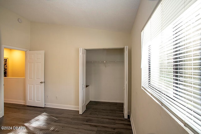 unfurnished bedroom with vaulted ceiling, a textured ceiling, a closet, and dark hardwood / wood-style flooring