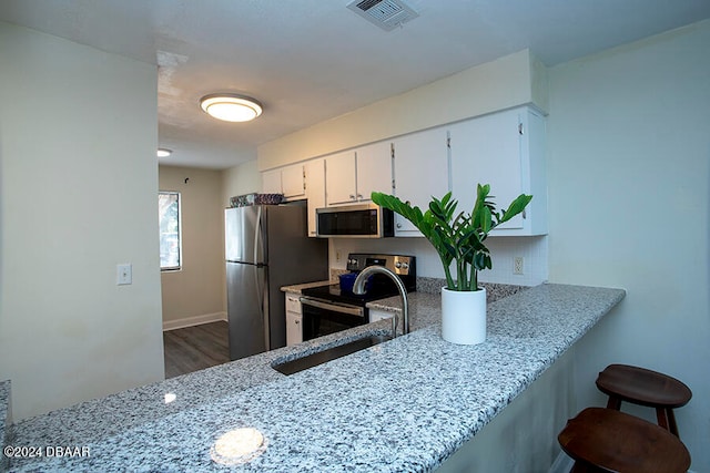 kitchen featuring white cabinetry, appliances with stainless steel finishes, dark hardwood / wood-style floors, and light stone counters