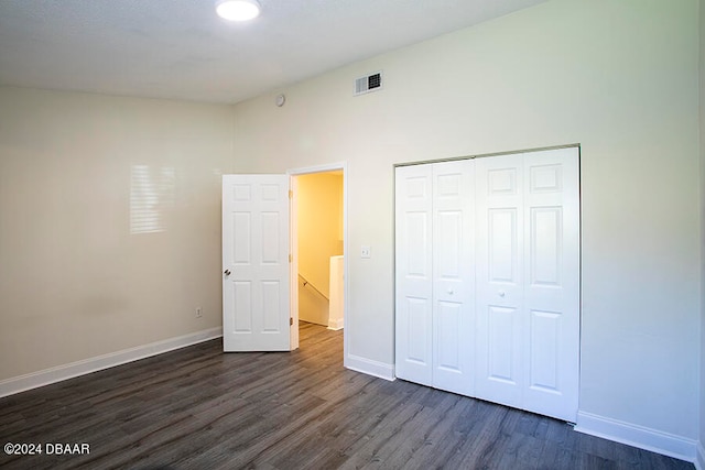 unfurnished bedroom with a high ceiling, a closet, and dark hardwood / wood-style floors