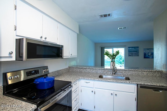 kitchen with kitchen peninsula, sink, light stone countertops, white cabinetry, and appliances with stainless steel finishes