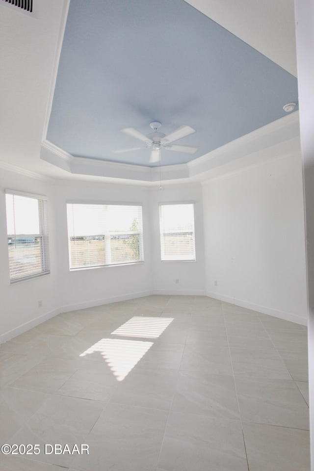 empty room with a raised ceiling, light tile patterned floors, ceiling fan, and a wealth of natural light