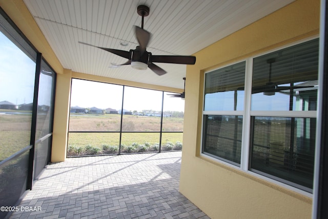 unfurnished sunroom featuring ceiling fan and a rural view