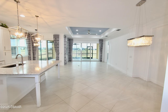 kitchen featuring a breakfast bar area, a tray ceiling, hanging light fixtures, light stone counters, and sink