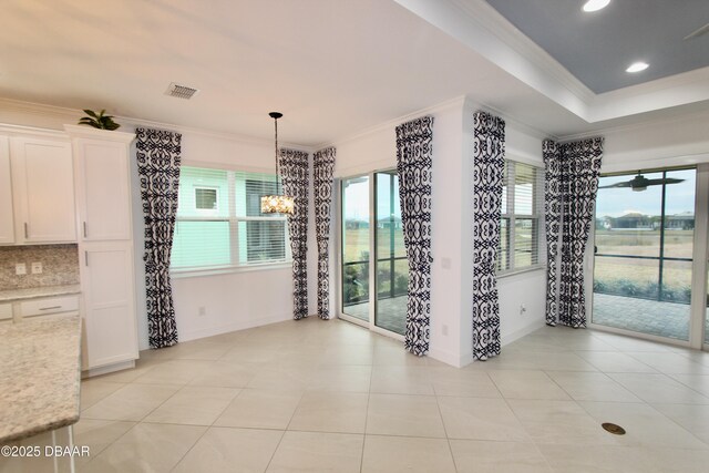 unfurnished dining area with light tile patterned floors, crown molding, and an inviting chandelier